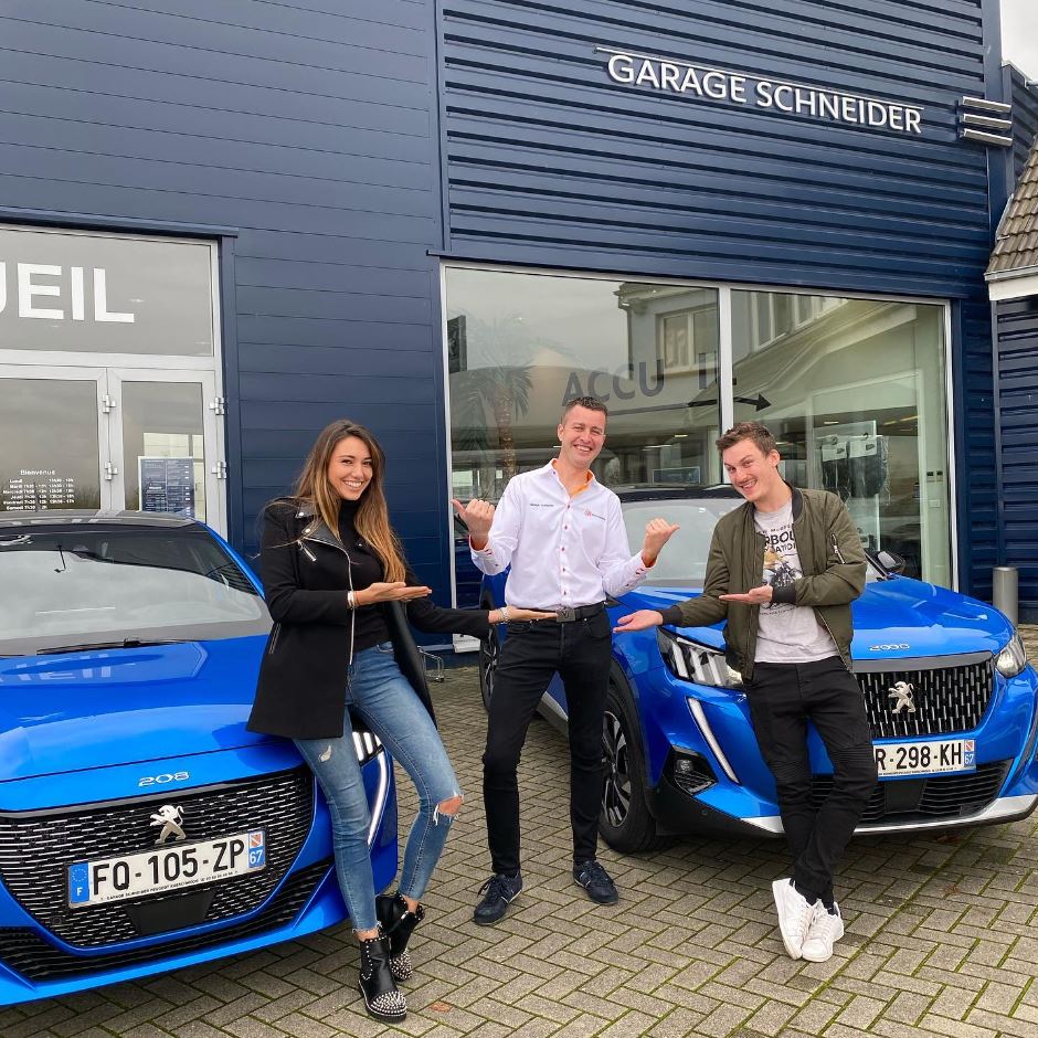 Trois personnes souriantes posant devant des voitures Peugeot bleues au Garage Schneider.
